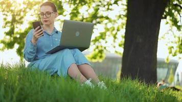 ocupado mujer trabajando a el ordenador portátil y utilizando teléfono inteligente en el parque