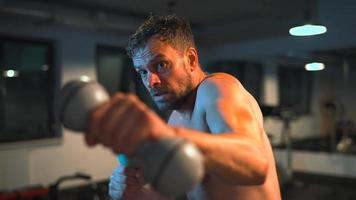 Boxer practicas puñetazos con pesas en su manos en el gimnasio en el noche. video