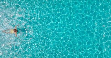 Aerial view of a woman in yellow swimsuit swimming in the pool. Summer lifestyle video