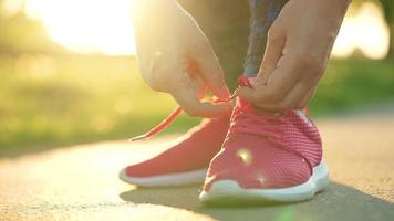 Woman tying shoelaces while jogging or walking at sunset. Slow motion video