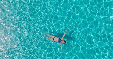 Top down view of a woman in a blue swimsuit lying on her back in the pool. video