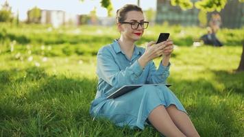 mulher usando Smartphone enquanto sentado dentro parque depois de acabamento ao ar livre trabalhos video