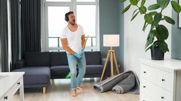 Man in headphones cleaning the house and having fun with a broom. video