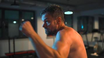 Alone boxer is working out blows on a punching bag in a gym in evening video