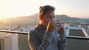 mujer empieza su día con un taza de té o café en el balcón a amanecer video