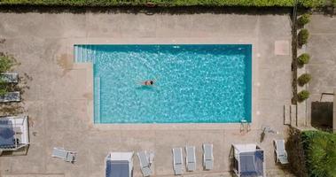 Aerial view of a woman in red swimsuit swimming in the pool. Summer lifestyle video