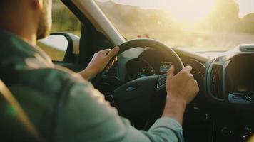 homem drives uma carro ao longo a estrada, a configuração Sol brilha dentro a parabrisa. video