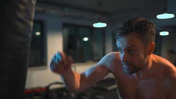 Alone boxer is working out blows on a punching bag in a gym in evening video