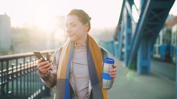 vrouw wandelen in een ijzig zonnig ochtend, drinken koffie en gebruik makend van smartphone video