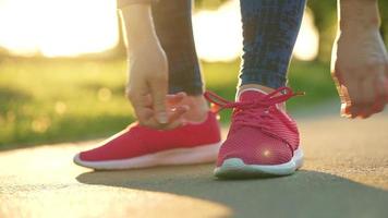 Woman tying shoelaces while jogging or walking at sunset. Slow motion video