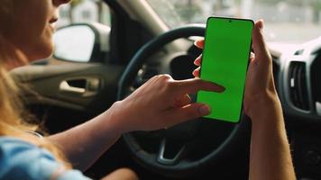 kvinna förare använder sig av en smartphone inuti de bil. Chromakey smartphone med grön video
