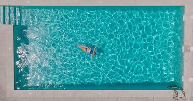 Top down view of a woman in a blue swimsuit lying on her back in the pool. video