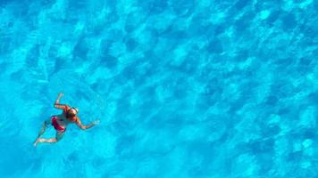 aéreo ver de un mujer en rojo traje de baño nadando en el piscina. verano estilo de vida