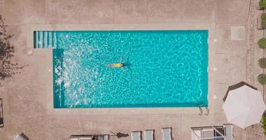 parte superior abajo ver de un mujer en un amarillo traje de baño acostado en su espalda en el piscina. video