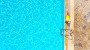 Top view of a woman in yellow swimsuit and a hat sits on the edge of the pool video