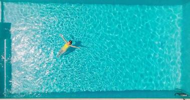 Top down view of a woman in an yellow swimsuit lying on her back in the pool. video