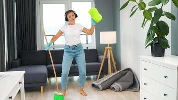 mulher dentro fones de ouvido limpeza a casa e tendo Diversão dançando com uma vassoura video