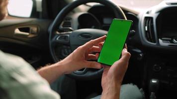 Male driver using a smartphone inside the car. Chromakey smartphone with green video