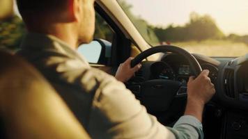 homem drives uma carro ao longo a estrada, a configuração Sol brilha dentro a parabrisa. video