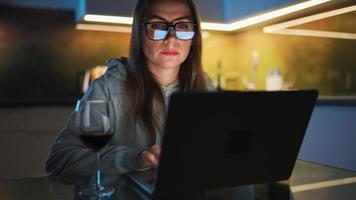 Woman is sitting in the kitchen and working on a laptop at night video