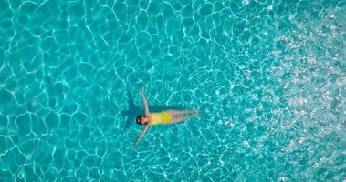 Top down view of a woman in an yellow swimsuit lying on her back in the pool.