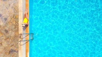parte superior ver de un mujer en amarillo traje de baño y un sombrero se sienta en el borde de el piscina video
