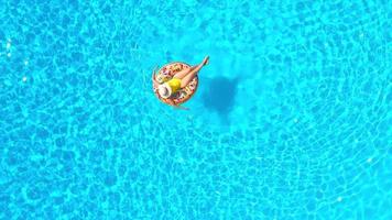 parte superior abajo ver de un mujer en amarillo traje de baño acostado en un rosquilla en el piscina