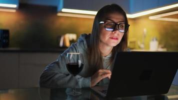 donna è seduta nel il cucina e Lavorando su un' il computer portatile a notte video