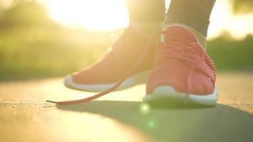 Woman tying shoelaces while jogging or walking at sunset. Slow motion video