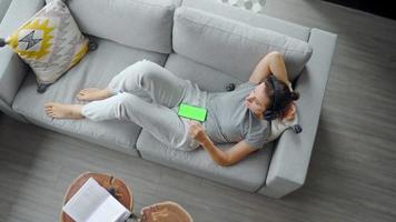 détendu femme dans écouteurs avec téléphone intelligent avec vert maquette écran video