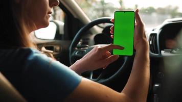 Female driver using a smartphone inside the car. Chromakey smartphone with green video