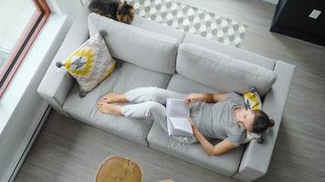 overhead visie van vrouw lezing de boek, aan het liegen Aan bankstel Bij huis video