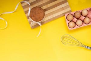 Easter pastries on the table with chicken eggs and a whisk on a yellow background. Top view photo