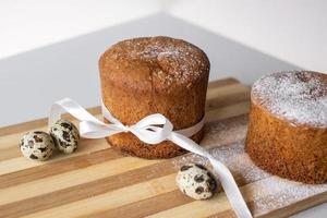 Easter pastries. Quail eggs are lying near an Easter cake with a white ribbon on a wooden board photo