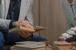 un hombre y un mujer sentar a un mesa y Mira mediante libros juntos, un profesor y un estudiante leer educativo literatura, preparar para un conferencia, escribir un tesis foto