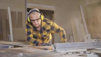 mannetje timmerman is snijdend spaanplaat met elektrisch tafel zag in werkplaats. timmerman Mens gebruik makend van kettingzaag bezuinigingen planken. video