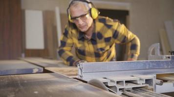 Male carpenter working in carpentry factory cutting boards with saw. Adult carpenter man cutting wood on table saw. video