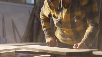 das Zimmermann weht das Staub auf das hölzern Planke im das Werkstatt. das Zimmermann weht auf das staubig hölzern Planke weht das Staub und nimmt Messungen auf das Holz. video