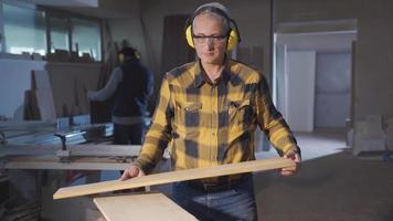 Skilled and experienced carpenter man looking at camera. Male carpenter holding wood in workshop looking at camera and smiling. video