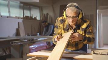 adulto carpinteiro homem trabalhando dentro carpintaria oficina medidas madeira com metro. masculino carpinteiro medindo empoeirado madeira com metro e marcação com lápis. video