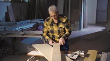 Carpenter man measuring wooden boards with meter. The carpenter carefully examines the timber on the table and measures it with the meter. video