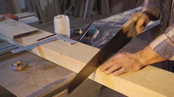 Close-up carpenter is cutting wood with a handsaw. Carpenter cuts timber with handsaw in carpentry workshop. video