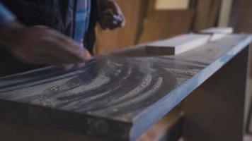 The carpenter is measuring the wood with a meter on his dusty workbench. The man who dusts the bench makes the measurement with the meter and marks the measured place with the pen. video