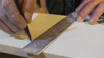 de cerca carpintero manos medición madera con regla en taller. carpintero medición madera con regla en polvoriento banco mesa y calificación con lápiz. video