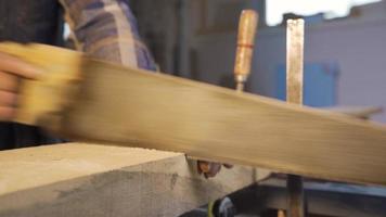 Male carpenter is cutting wooden plank with saw. Close-up carpenter is cutting wooden plank with a handsaw.