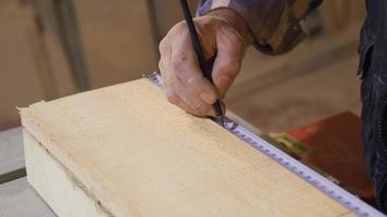 Nahansicht von zerknittert Zimmermann Hände Messung Holz mit Meter. Senior Zimmermann Hände messen roh Holz mit Lineal und Kennzeichen mit Bleistift. video