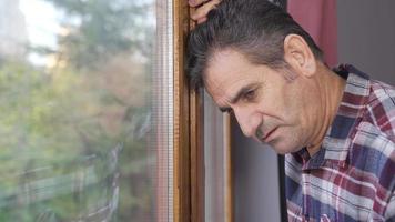 Deprimido hombre mira fuera de por el ventana. el hombre es a hogar acecho fuera el ventana y es considerado. video