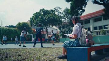 a female student is sitting in the school yard with a background of people playing basketball video
