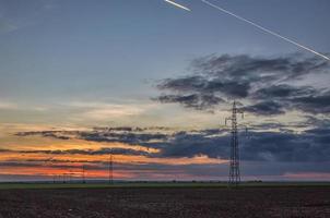 Poles and overhead power lines silhouettes in the dusk. Electricity generation and distribution. Electric power industry and nature concept photo