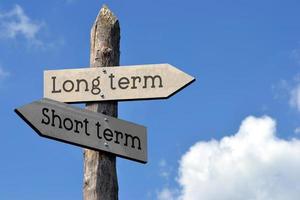 Short or Long Term - Wooden Signpost with Two Arrows, Sky with Clouds photo